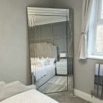 Decorative frameless wall mirror. Positioned in the bedroom. Full length mirror leaning against the wall. Shop online and delivered to your home.
