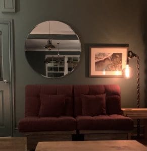 Round Bordeaux mirror, wall mounted in the living room above the sofa. Glass mirror features a bevel edge.