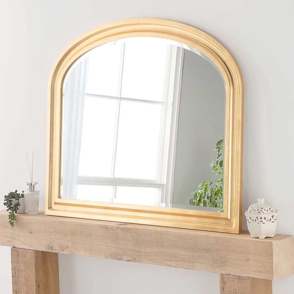 Gold overmantle mirror. Positioned in the living room lounge, leaning on the fire place mantle against a wall.
