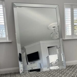 Extra large frameless wall mirror. Venetian style silver mirror positioned in the living room leaning against the wall. Features a raised edge all glass frame.