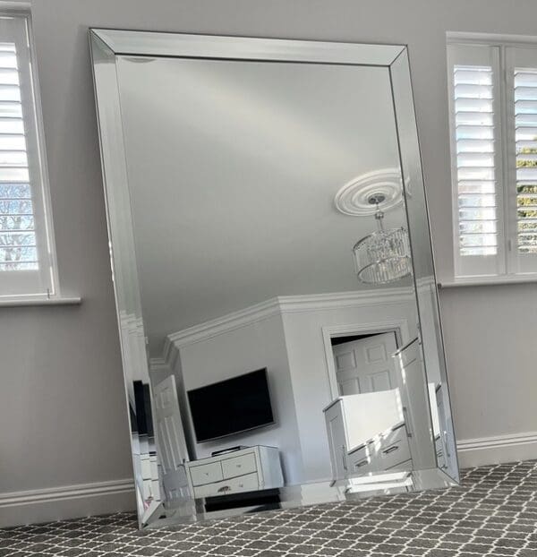 Extra large frameless wall mirror. Venetian style silver mirror positioned in the living room leaning against the wall. Features a raised edge all glass frame.